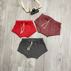 May include: Three pairs of shorts in different colors: red, burgundy, and gray. Each pair has a drawstring waist.