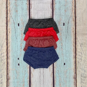 May include: Four pairs of knit shorts in different colors: dark gray, red, burgundy, and navy blue. The shorts are stacked on top of each other.