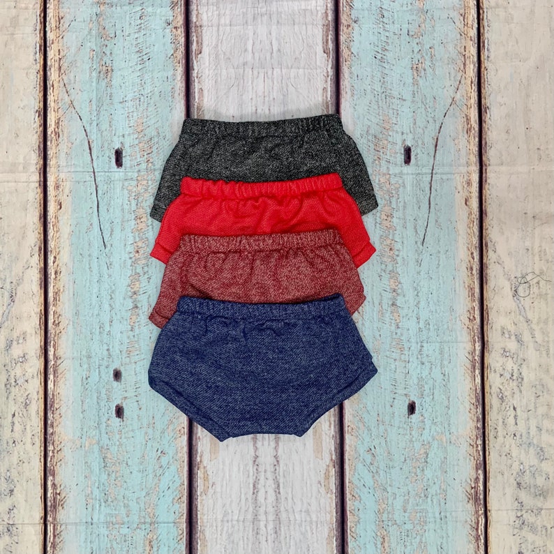 May include: Four pairs of knit shorts in different colors: dark gray, red, burgundy, and navy blue. The shorts are stacked on top of each other.