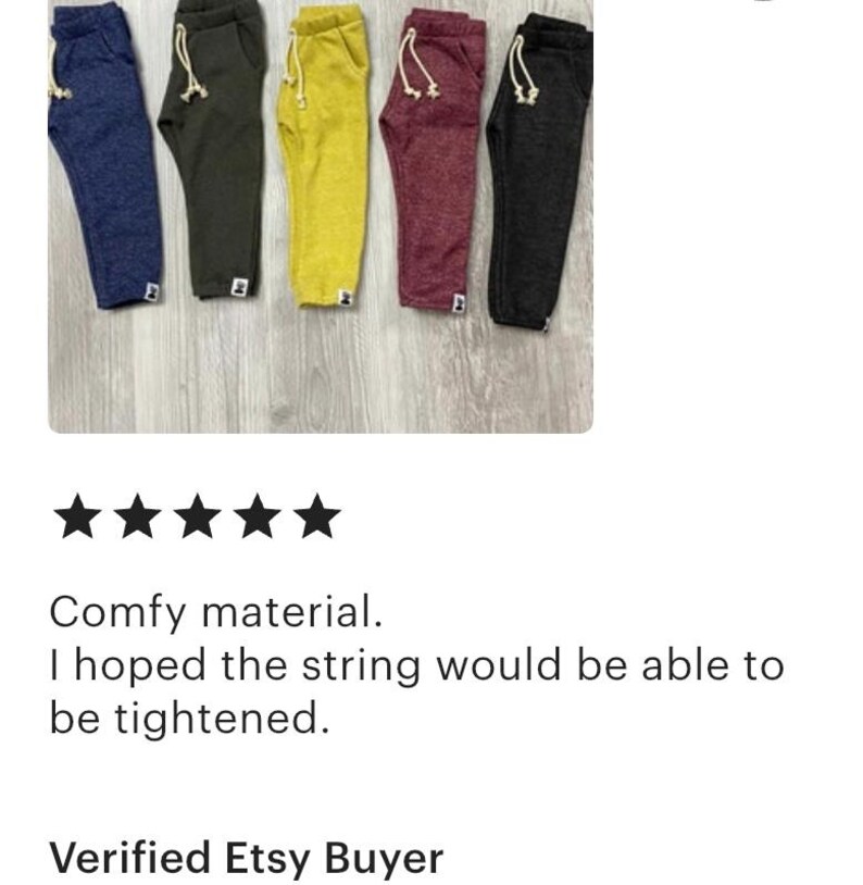 May include: Five pairs of sweatpants in navy, olive green, yellow, burgundy, and black. Each pair features a drawstring, pockets, and a small logo near the ankle. The trousers are displayed on a light wood-grain surface.