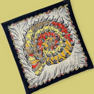 May include: Square silk scarf with a black border and a central design featuring a spiral of snails in shades of brown, yellow, and red. The scarf has a white border with black and red decorative elements.