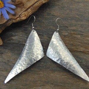 May include: A pair of silver triangle earrings with a hammered texture. The earrings have a simple, modern design.