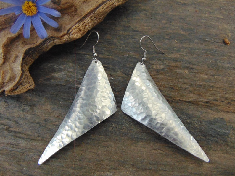 May include: A pair of silver triangle earrings with a hammered texture. The earrings have a simple, modern design.
