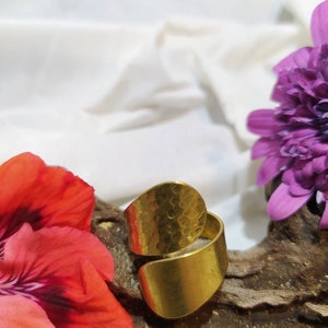 May include: A gold-toned hammered metal ring with a wide band. The ring is open and can be adjusted to fit different finger sizes.