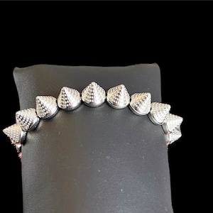 May include: Silver bracelet with a row of pointed cone-shaped charms.