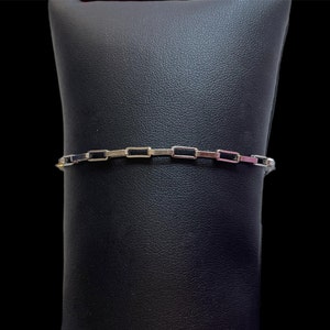 May include: A silver bracelet with a chain link design. The links are rectangular and have a black enamel finish.