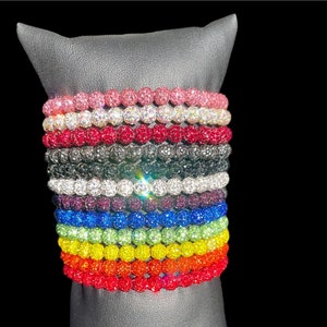 May include: A stack of colorful beaded bracelets with a variety of colors including pink, red, black, white, blue, green, yellow, and orange. The bracelets are stacked on a gray display stand.