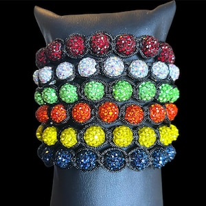 May include: A stack of colorful bracelets with black elastic bands and sparkly beads. The bracelets are arranged in a rainbow pattern, starting with red and ending with blue.