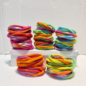 May include: A stack of colorful tie-dye fabric hair scrunchies in various colors, including orange, pink, green, and blue.