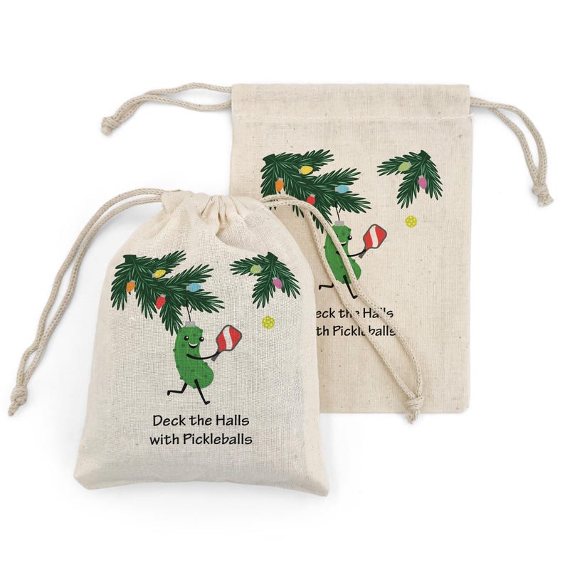 May include: Two beige drawstring bags with a festive pickleball theme. One bag features a cartoon pickle playing pickleball under a decorated Christmas tree, with the text "Deck the Halls with Pickleballs". The other bag has a similar design.