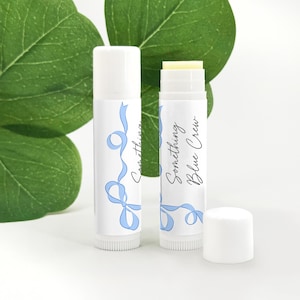 May include: Two white lip balm tubes with blue ribbon designs. The text on the tubes reads "Something Blue Crew".