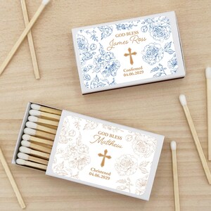 Puede incluir: Dos cajas de cerillas con dise&ntilde;os florales y texto personalizado. Una caja tiene detalles florales azules y dice "God Bless James Ross" con una cruz y una fecha. La otra tiene detalles florales dorados y dice "God Bless Matthew" con una cruz y una fecha.