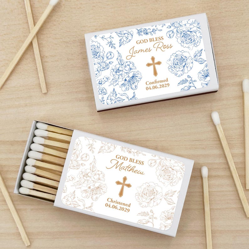 Puede incluir: Dos cajas de cerillas con dise&ntilde;os florales y texto personalizado. Una caja tiene detalles florales azules y dice "God Bless James Ross" con una cruz y una fecha. La otra tiene detalles florales dorados y dice "God Bless Matthew" con una cruz y una fecha.