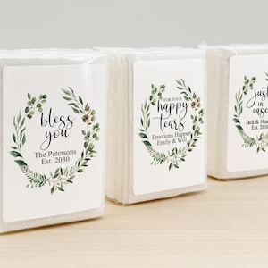 Peut inclure: Trois paquets de mouchoirs blancs avec des étiquettes décoratives. Les étiquettes présentent des couronnes botaniques et du texte tel que "bless you", "for your happy tears" et "just in case". Les noms et les dates sont également présents.