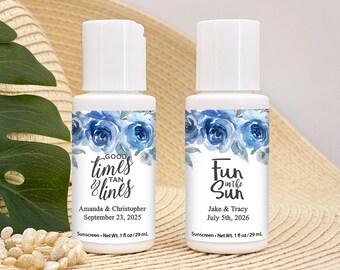 May include: Two white plastic bottles of sunscreen with blue floral labels. The left bottle says "Good times & tan lines" with the names Amanda & Christopher and the date September 23, 2025. The right bottle says "Fun in the Sun" with the names Jake & Tracy and the date July 5th, 2026. Both bottles say "Sunscreen - Net Wt. 1 fl oz/29 ml."