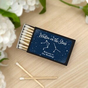 May include: A black matchbox with a navy blue label featuring a constellation design and the text "Written in the Stars" and "Welcome to Our Wedding!"