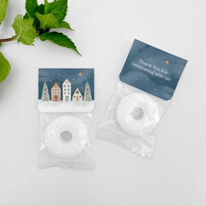 May include: Two clear plastic bags containing white round mints. One bag features a header card with a winter village illustration and stars. The other bag has a dark blue header card with the text "Thank You For Celebrating with us!" and gold stars.