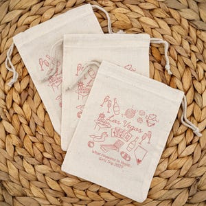 Natural color cotton bags with drawstring top with a Las Vegas doodle design representing a disco ball, playing cards, Vegas sign, pool floats, and other pool related icons.  Includes two lines of custom text.