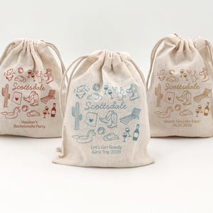 May include: Three beige drawstring bags with the word "Scottsdale" and various southwestern-themed illustrations. The bags have different text, including "Heather's Bachelorette Party," "Anna's Tying the Knot! 04.25.2029," and "Let's Get Rowdy Girls Trip 2029."