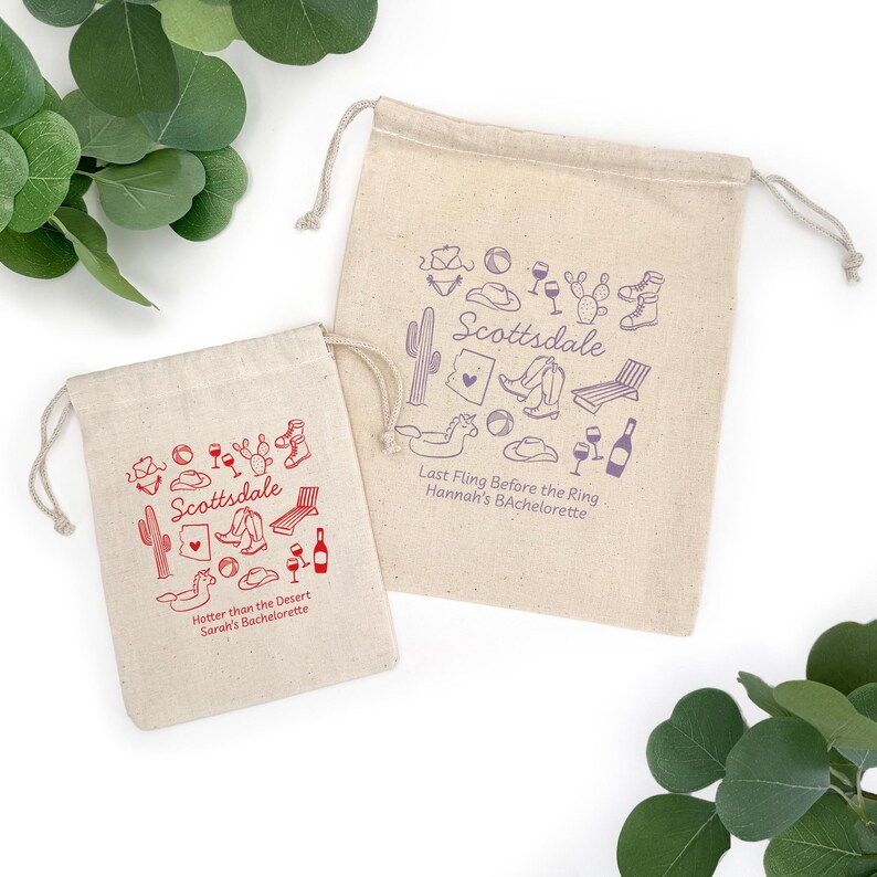 May include: Two beige drawstring bags with red and purple illustrations and text. The bags feature drawings of cacti, cowboy boots, and wine glasses. The text on the bags reads "Scottsdale" and "Hotter than the Desert Sarah's Bachelorette" and "Last Fling Before the Ring Hannah's Bachelorette."
