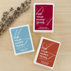 May include: Three rectangular tissue packets in burgundy, dusty blue, and terracotta, each featuring a large script letter, the text FOR YOUR HAPPY TEARS, and personalised names and dates. A sprig of dried lavender is positioned to the left.