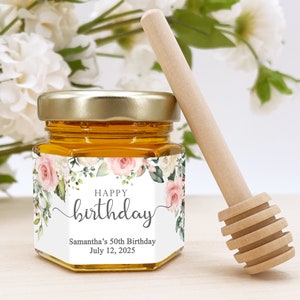 May include: A small glass jar filled with honey, with a wooden honey dipper. The jar has a white label with pink and white floral designs and the text "Happy birthday", "Samantha's 50th Birthday", and "July 12, 2025".