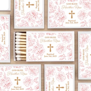 May include: White matchboxes with floral designs and the text "GOD BLESS Heather Rose" and "Baptized June 3rd, 2029". The boxes feature a cross and are surrounded by a floral pattern. The matches are visible in an open box.
