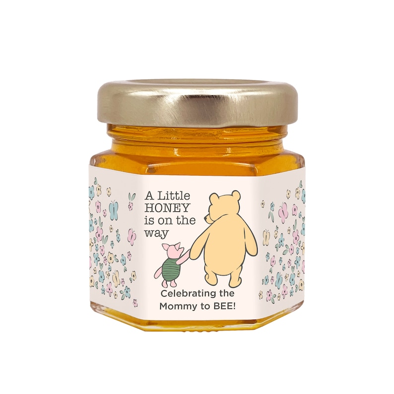 May include: A small glass jar of honey with a Winnie the Pooh and Piglet themed label. The label says "A Little Honey is on the way. Celebrating the Mommy to BEE!" with a floral pattern.