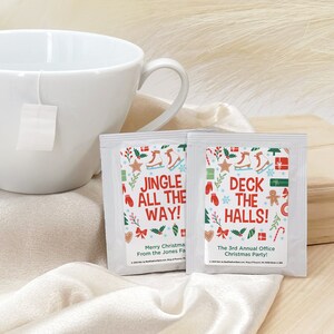 May include: Two white tea bags with festive Christmas designs. One bag features the text "Jingle All The Way!" and the other bag features the text "Deck The Halls!" Both bags have a red, green, and white color scheme with illustrations of Christmas ornaments, candy canes, and snowflakes.