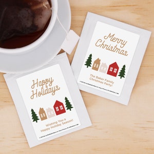 May include: Two white tea bags with festive Christmas designs. One bag features a red house with the text "Happy Holidays" and the other features a red house with the text "Merry Christmas". Both bags have a small illustration of houses and trees.
