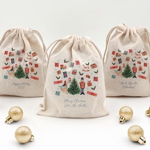May include: Three beige drawstring gift bags with Christmas-themed illustrations. Each bag features a Christmas tree, nutcracker, and various gift boxes. Text on the bags includes "Happy Holiday 2029", "Merry Christmas Love, The Smiths", and "Thank You For Celebrating!"