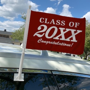 Puede incluir: Una bandera de ventana de coche roja con texto blanco que dice "Clase de 20XX ¡Felicidades!"