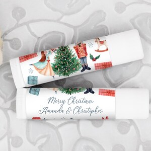 May include: Two white tubes with Christmas themed labels. The top label features a nutcracker, a rocking horse, and a Christmas tree. The bottom label says "Merry Christmas Amanda & Christopher".