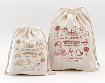 Può includere: Due sacchetti beige con coulisse con illustrazioni marroni di monumenti di Savannah. Le borse presentano disegni di un tram, un pianoforte e tazze di caffè. Una borsa dice "Peachy Keen Madison's Bachelorette" e l'altra dice "Thank You For Coming Jack & Chloe".