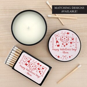 May include: A pink and white candle with a black lid and a matching box of matches. The candle and matchbox have a red design with a heart-shaped cake, wine glasses, and a bottle of wine. The text on the candle and matchbox reads "Happy Valentine's Day! - Olina".