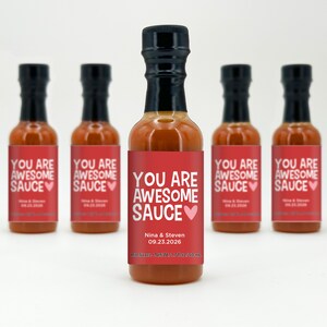 May include: Six small bottles of hot sauce with red labels that say "You are awesome sauce" with a pink heart. The labels also include the names "Nina & Steven" and the date "09.23.2026".