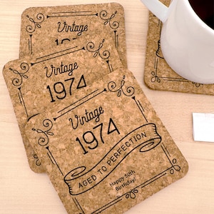 May include: Set of four cork coasters with black text and a decorative border. The coasters feature the text "Vintage 1974" and "Aged to Perfection".