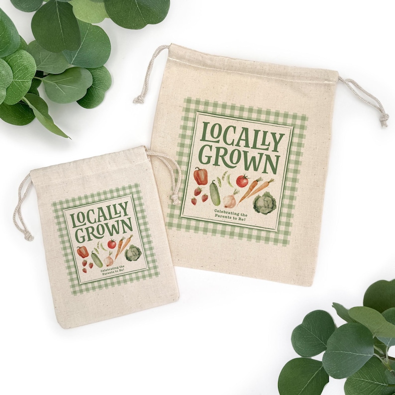 May include: Two beige drawstring bags with a green gingham border and the words "Locally Grown" printed on them. The bags feature illustrations of vegetables and the text "Celebrating the Parents to Be!"