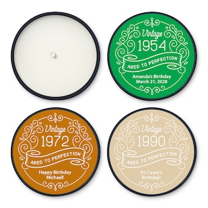 May include: A candle with a black rim and a white wax interior is shown next to three round labels. The labels have a vintage design with the years 1954, 1972, and 1990, along with birthday messages.