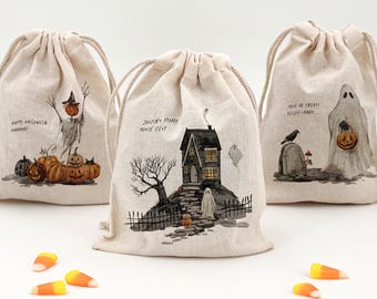 May include: Three off-white drawstring bags featuring watercolor-style Halloween illustrations. The bags display a scarecrow with pumpkins, a haunted house with the text "Justin's Spooky Movie Fest," and a ghost with "Trick or Treat! Reilly's Candy."