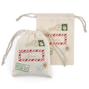 May include: Two beige drawstring gift bags with holiday-themed postage stamp designs. One bag reads "Deliver to: James" in a red frame. The other bag reads "Deliver to: Kristina". Both bags have a "Do Not Open Until Dec. 25th" stamp.