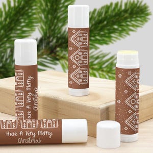 Puede incluir: Cuatro tubos de bálsamo labial blancos con etiquetas marrones que presentan un diseño de casa de jengibre y el texto "Have A Very Merry Christmas".