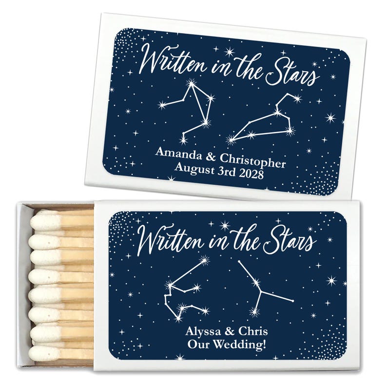 May include: Two white matchboxes with blue labels. The labels feature a dark blue background with white stars and constellations. The text on the labels reads "Written in the Stars" and includes the names of the couples and the date of their wedding.