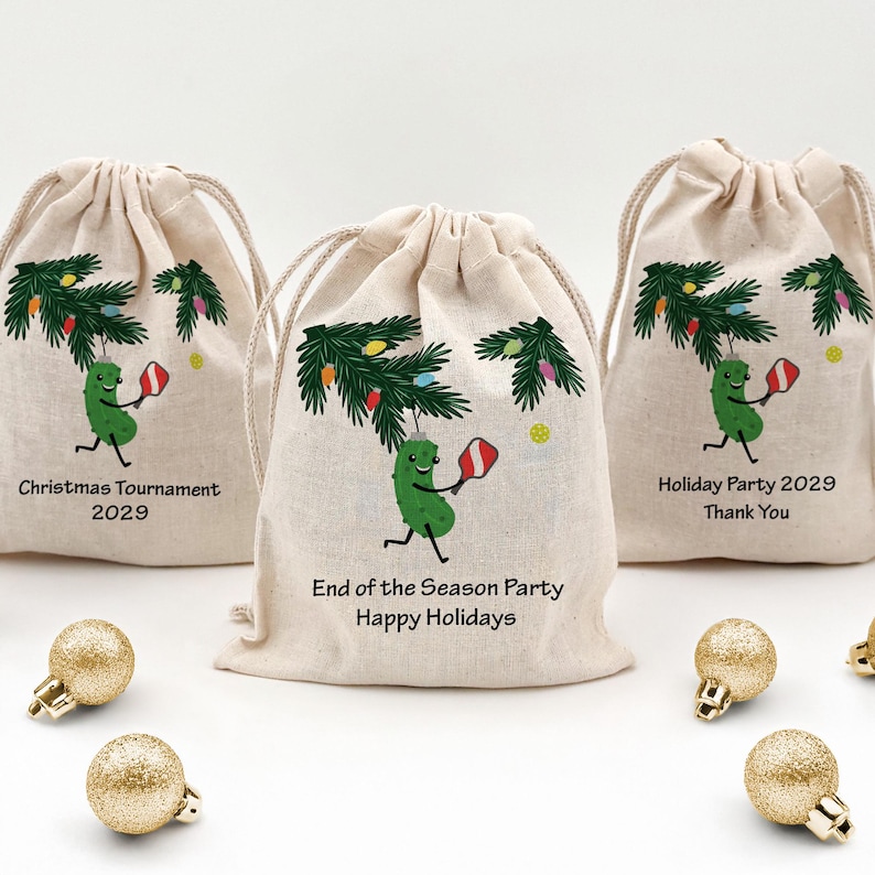 Three mini drawstring bags for the holiday season with a hanging pickle from a Christmas tree branch.  The pickle is holding a pickleball paddle and has two lines of custom text for your event.