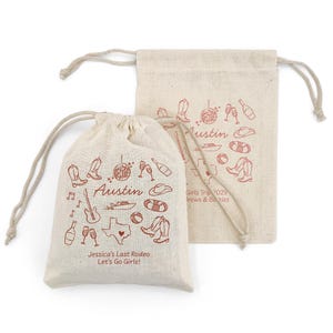 May include: Two beige drawstring bags with red illustrations and text. One bag features the word "Austin", a Texas outline, cowboy boots, and other icons. The text "Jessica's Last Rodeo Let's Go Girls!" is also visible. The second bag has similar illustrations.