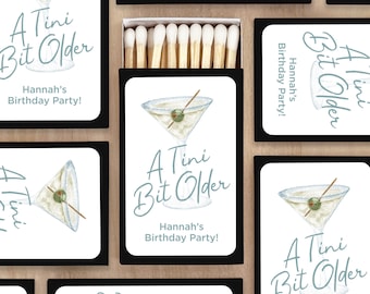 May include: A set of matchboxes with a white background and black trim. Each box features a martini glass with an olive and a stick, and the text "A Tini Bit Older" in blue script. The text "Hannah's Birthday Party!" is also included in black text.