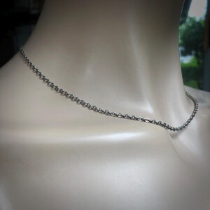 May include: A silver-colored chain necklace draped around a mannequin's neck. The chain is made of small, interconnected links, creating a delicate and simple design. The necklace is a classic accessory.