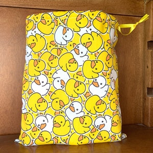 May include: A yellow drawstring bag with a repeating pattern of cartoon ducks in yellow and white. The bag is tied with a yellow ribbon. The bag is made of fabric.