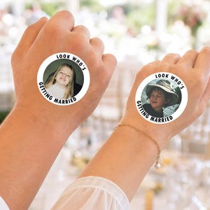 May include: Two circular temporary tattoos featuring black text that reads LOOK WHO'S GETTING MARRIED around the perimeter. Each tattoo displays a different childhood photograph of a person, one showing a young girl and the other a young boy in a hat.