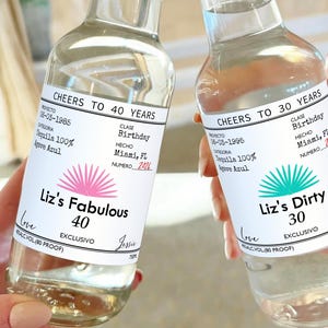 May include: Two clear glass bottles with personalized labels. The labels are white with black text and a pink and turquoise agave plant design. The text on the labels reads "Cheers to 40 Years" and "Liz's Fabulous 40" on one bottle and "Cheers to 30 Years" and "Liz's Dirty 30" on the other bottle.